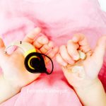 Description de la photo. Une petite fille tient un implant cochléaire dans la main gauche et un appareil auditif de l'autre main. Fin de la description de la photo.